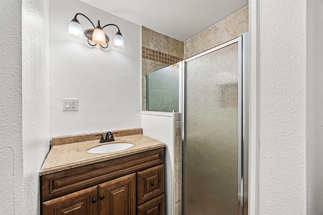 bathroom with a textured ceiling, a textured wall, a shower stall, and vanity