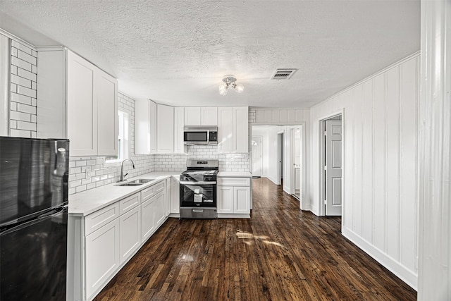 kitchen featuring dark wood-style flooring, stainless steel appliances, visible vents, white cabinets, and a sink