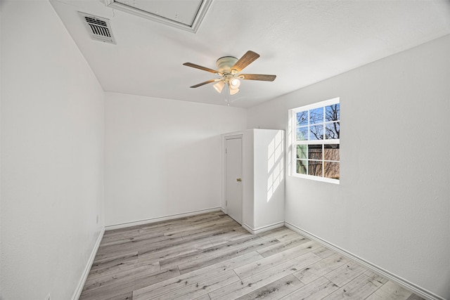 unfurnished room featuring visible vents, light wood-style flooring, attic access, a ceiling fan, and baseboards