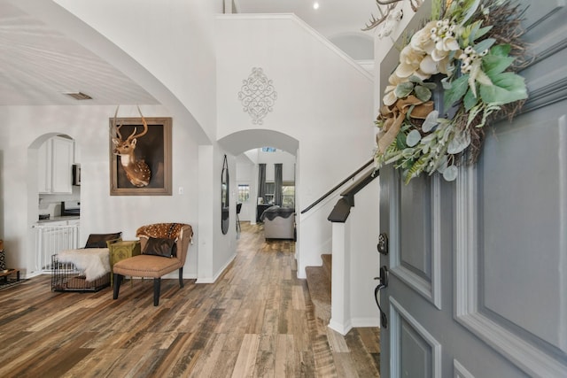 foyer with arched walkways, a high ceiling, wood finished floors, visible vents, and stairway