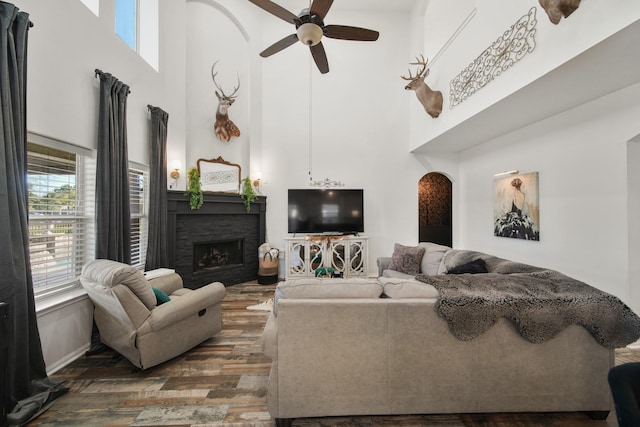 living room with arched walkways, ceiling fan, a stone fireplace, and wood finished floors