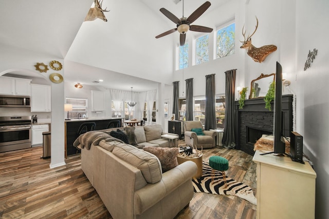 living area featuring a high ceiling, a fireplace, wood finished floors, and a ceiling fan