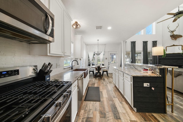 kitchen with a breakfast bar area, stainless steel appliances, visible vents, white cabinetry, and a sink