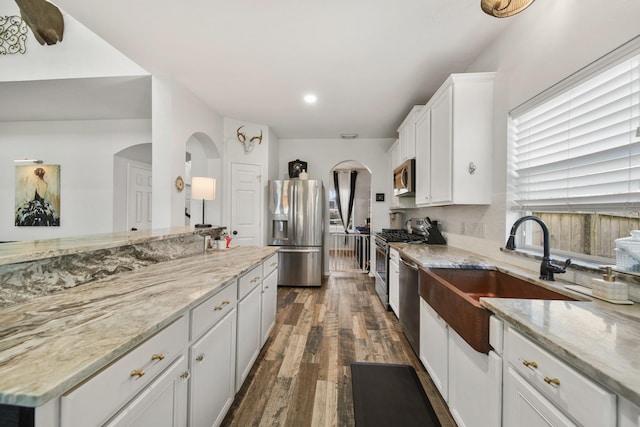 kitchen with light stone counters, arched walkways, dark wood finished floors, stainless steel appliances, and white cabinetry