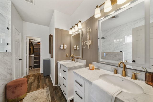 bathroom with two vanities, visible vents, a sink, wood finished floors, and a walk in shower