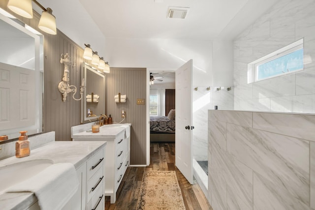 ensuite bathroom with ensuite bathroom, a walk in shower, two vanities, wood finished floors, and visible vents