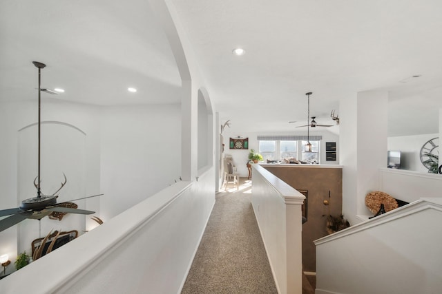 hallway featuring carpet floors, recessed lighting, arched walkways, and an upstairs landing