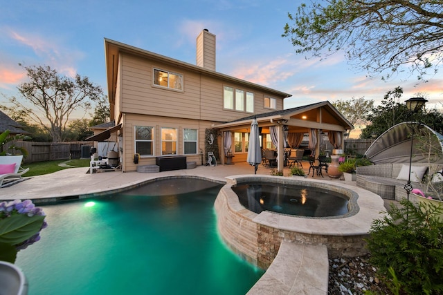 rear view of property featuring a fenced backyard, a chimney, a pool with connected hot tub, and a patio