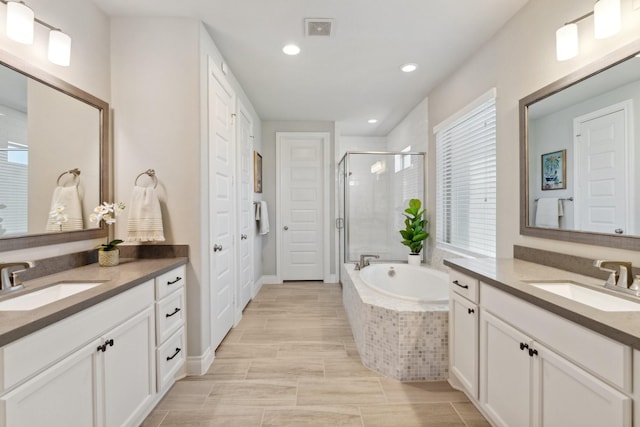 full bathroom featuring a garden tub, a stall shower, two vanities, and a sink