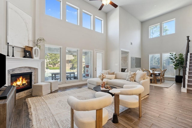 living area featuring stairway, plenty of natural light, a stone fireplace, and wood finished floors