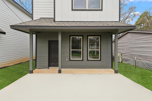 doorway to property with board and batten siding, a shingled roof, and a lawn