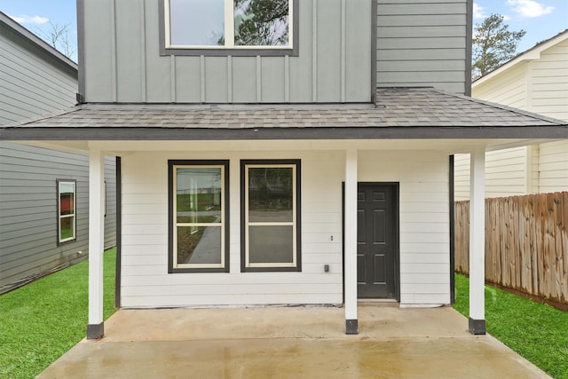 property entrance featuring a shingled roof, fence, board and batten siding, and a yard