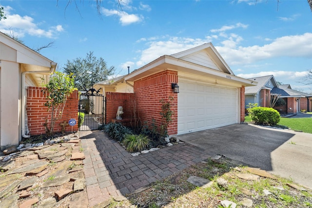 view of side of property featuring driveway, an attached garage, a gate, and brick siding