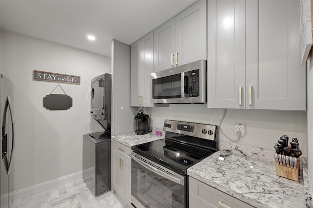 kitchen with baseboards, stacked washer / dryer, light stone counters, marble finish floor, and stainless steel appliances