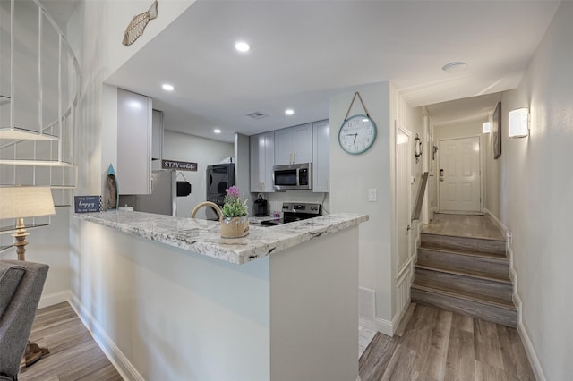 kitchen featuring baseboards, wood finished floors, light stone countertops, stainless steel appliances, and recessed lighting