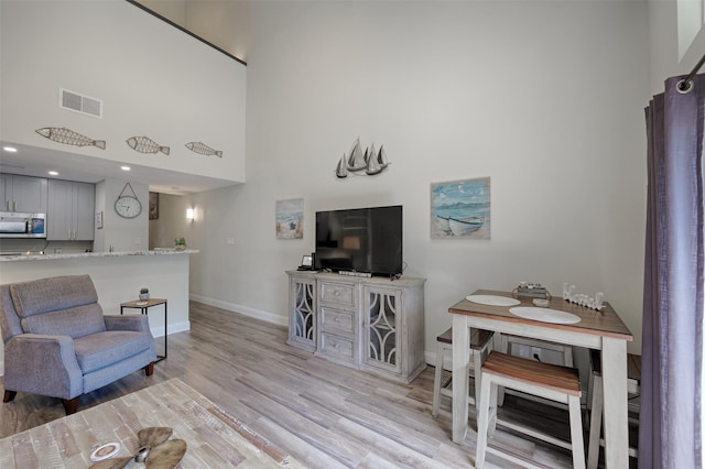 living room featuring visible vents, baseboards, light wood-style flooring, a high ceiling, and recessed lighting