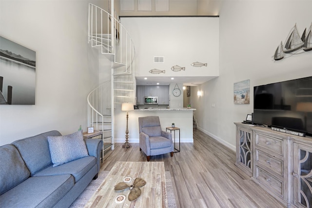 living area featuring visible vents, stairway, a towering ceiling, light wood-style floors, and baseboards