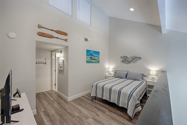 bedroom with a high ceiling, visible vents, baseboards, and wood finished floors