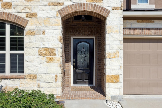 view of exterior entry with a garage, stone siding, and brick siding