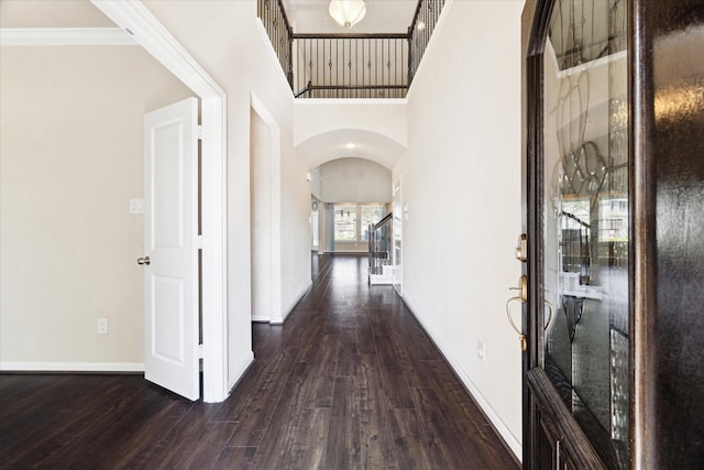 hall with arched walkways, a high ceiling, wood finished floors, baseboards, and stairs