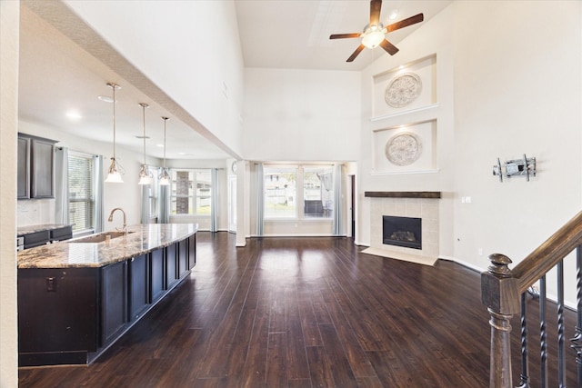 living room with a towering ceiling, baseboards, a ceiling fan, dark wood-style floors, and a tiled fireplace