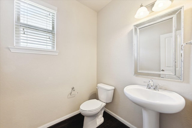 half bathroom featuring a sink, toilet, baseboards, and wood finished floors