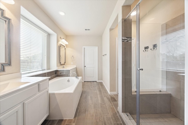 full bathroom featuring two vanities, visible vents, a shower stall, a bath, and wood tiled floor