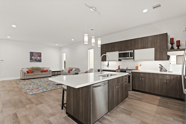 kitchen featuring a kitchen island with sink, stainless steel appliances, dark brown cabinets, light countertops, and decorative backsplash