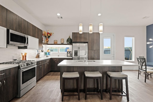 kitchen with a breakfast bar area, stainless steel appliances, tasteful backsplash, light countertops, and dark brown cabinets