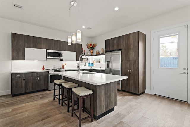 kitchen with appliances with stainless steel finishes, a sink, light countertops, dark brown cabinets, and backsplash