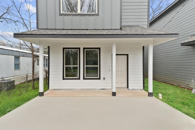 view of exterior entry with board and batten siding, central AC, and a shingled roof