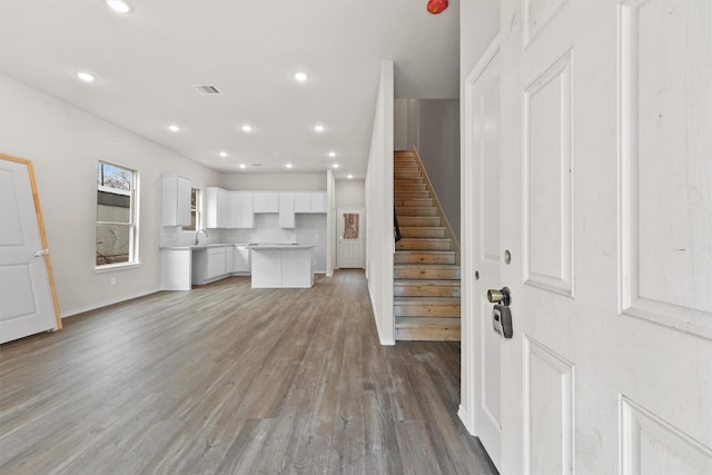 unfurnished living room with baseboards, visible vents, stairway, wood finished floors, and recessed lighting