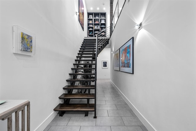 stairway featuring baseboards, a high ceiling, and tile patterned floors