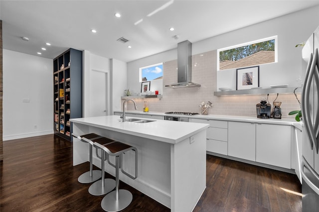 kitchen featuring a sink, visible vents, wall chimney range hood, an island with sink, and modern cabinets