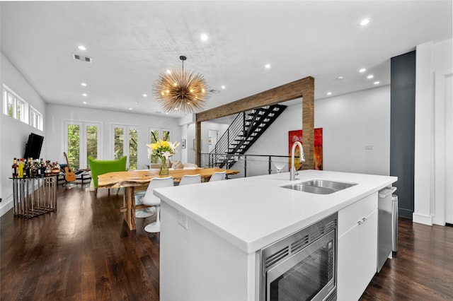 kitchen with a kitchen island with sink, dark wood-style flooring, a sink, visible vents, and appliances with stainless steel finishes