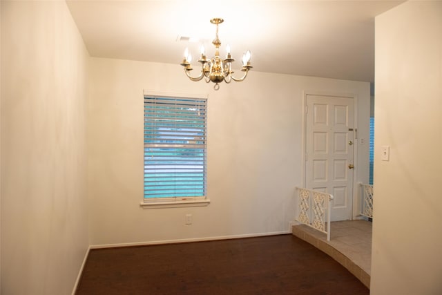 empty room with an inviting chandelier, baseboards, and wood finished floors