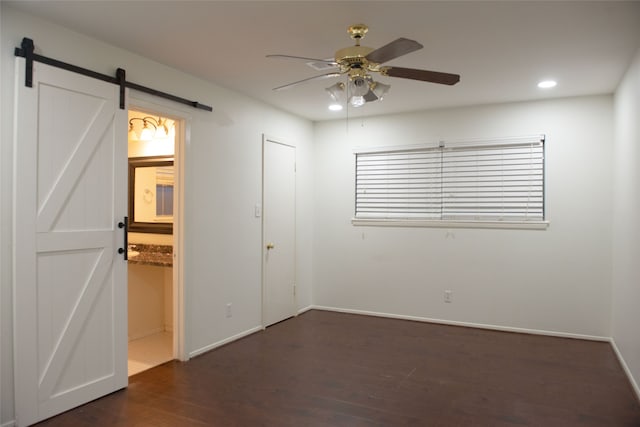 unfurnished bedroom featuring a barn door, baseboards, dark wood finished floors, and recessed lighting