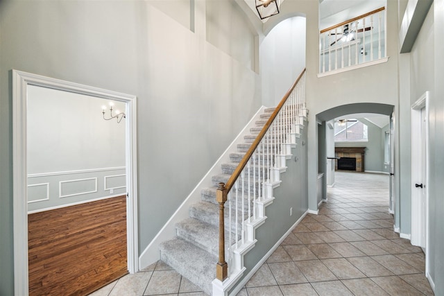 stairway with tile patterned floors, arched walkways, a fireplace, baseboards, and a towering ceiling