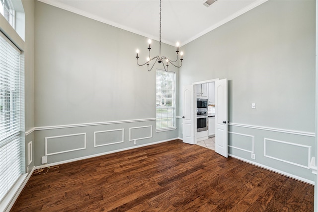 unfurnished dining area featuring a notable chandelier, wood finished floors, a wainscoted wall, and ornamental molding