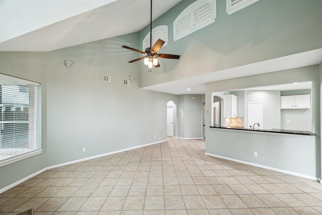 unfurnished living room with arched walkways, visible vents, baseboards, and ceiling fan