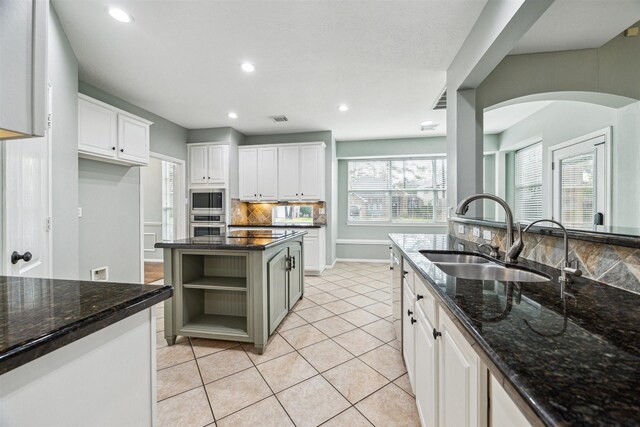 kitchen with a sink, appliances with stainless steel finishes, white cabinets, light tile patterned floors, and decorative backsplash