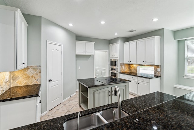 kitchen featuring a sink, stainless steel microwave, white cabinets, and light tile patterned floors