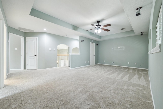 carpeted spare room featuring baseboards, a raised ceiling, visible vents, and a ceiling fan