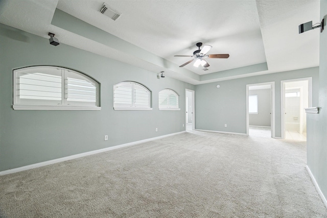 carpeted spare room featuring visible vents, a ceiling fan, a textured ceiling, baseboards, and a raised ceiling