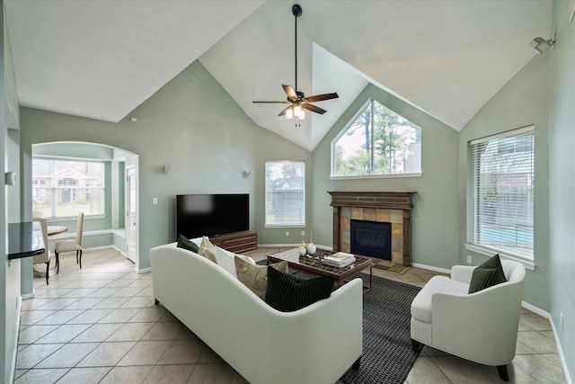 living area featuring ceiling fan, baseboards, a tiled fireplace, light tile patterned floors, and arched walkways