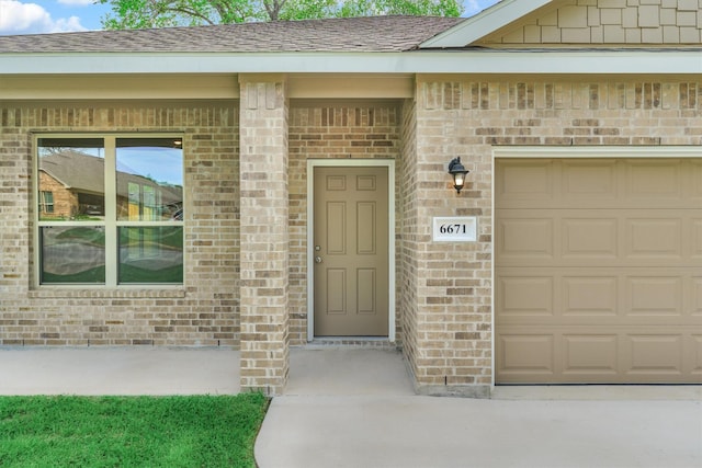 property entrance with brick siding, a shingled roof, and a garage