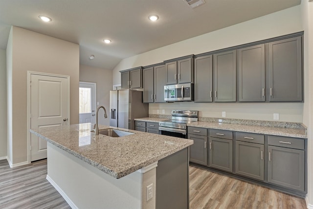 kitchen featuring light wood-type flooring, an island with sink, light stone counters, appliances with stainless steel finishes, and a sink