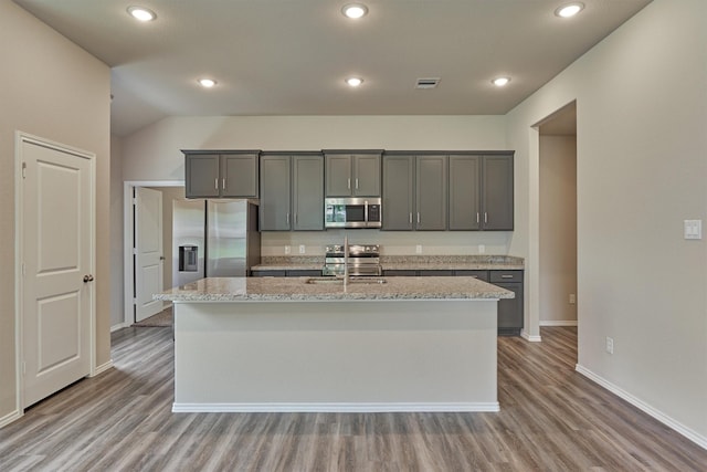 kitchen with a sink, stainless steel appliances, light wood-type flooring, and a kitchen island with sink