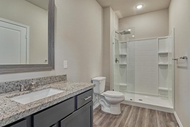 bathroom featuring vanity, wood finished floors, baseboards, tiled shower, and toilet