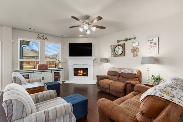 living room featuring a ceiling fan, a lit fireplace, visible vents, and wood finished floors